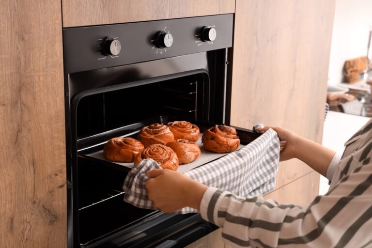 Woman,Taking,Baking,Tray,With,Buns,From,Oven,In,Kitchen,